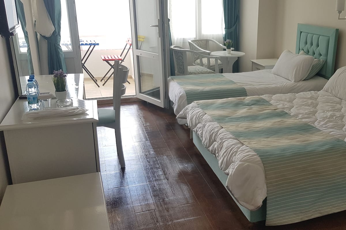 Una habitación de hotel con dos camas, una mesita, una silla y vistas al exterior.