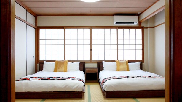 A traditional Japanese room with tatami flooring, two beds with white bedding, a wooden wardrobe, and a sliding shoji screen door. - Kujo no Yado Great House Osaka (Osaka)
