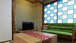 A modern living room with a wooden coffee table, a green sofa, a flat-screen TV, and a large window with blue-tinted glass. - Kujo no Yado Great House Osaka (Osaka)