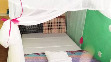 A single bed with a mosquito net, a pillow, and a folded towel.