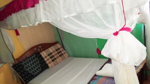 A bed with a white mattress, a colorful blanket, and a mosquito net. - Riverside Tourism Guest House (Embu)
