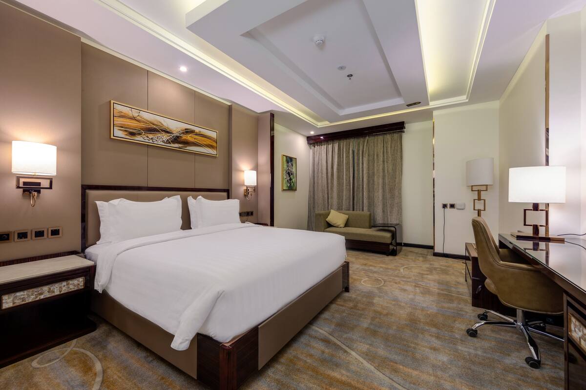 Habitación de hotel con una cama grande, un escritorio con una silla, un sofá y un cuadro en la pared.