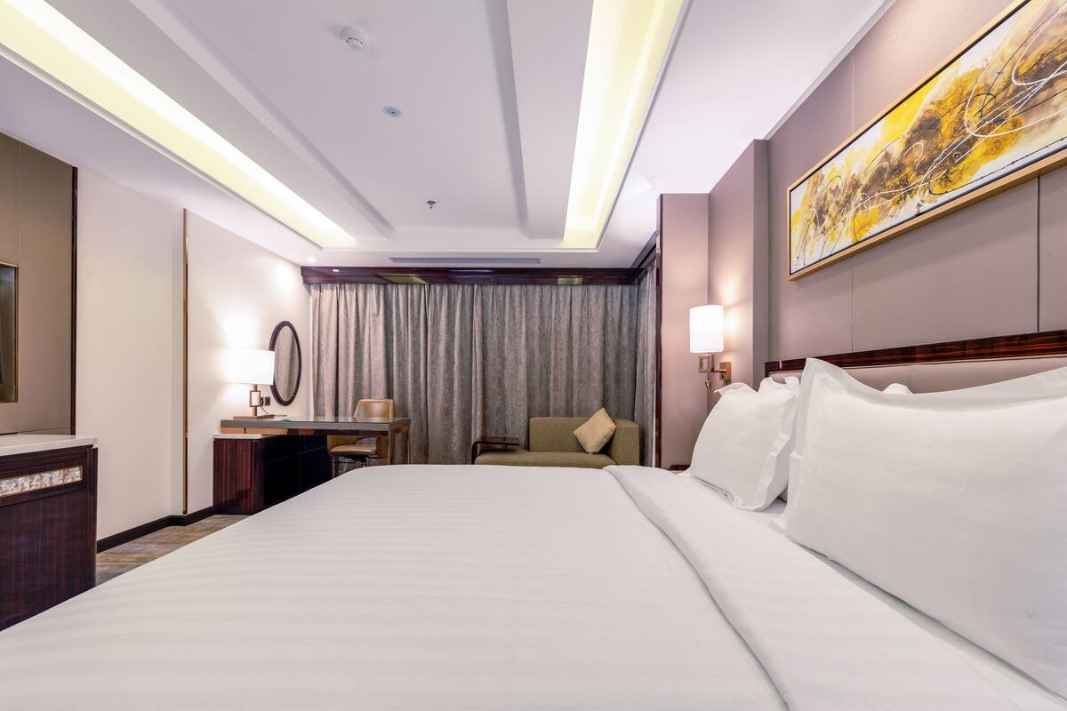 Habitación de hotel con una cama grande, un escritorio con lámpara, una silla y un cuadro grande en la pared.