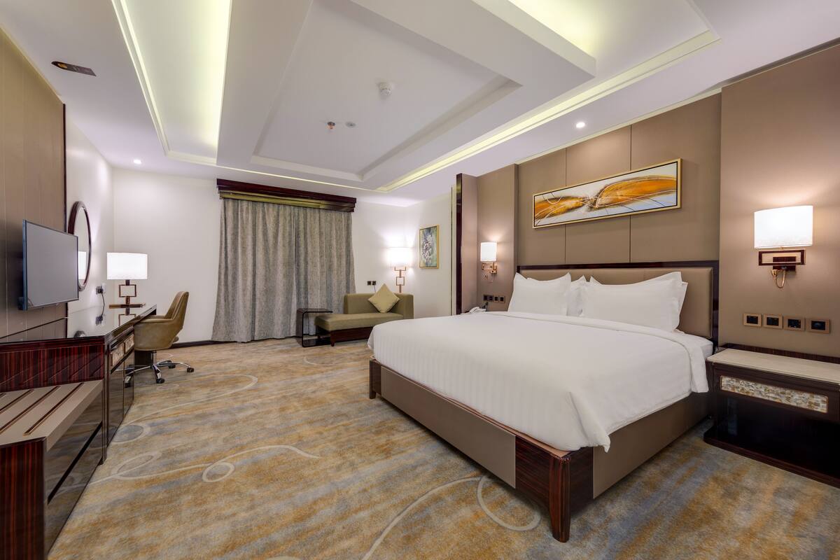 Habitación de hotel con una cama grande, un escritorio con silla, televisor y una lámpara de pared.