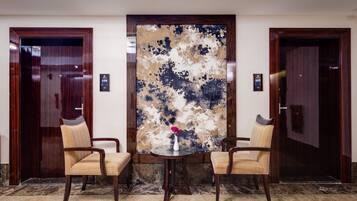 Un vestíbulo con dos puertas de madera, suelo de mármol y una mesa redonda con un florero.