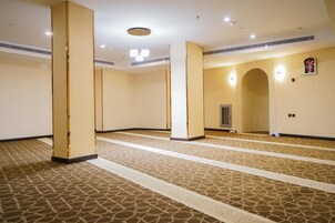 Un amplio vestíbulo de hotel con alfombra estampada, pilares grandes y una lámpara moderna.