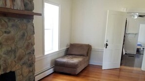 Ein Zimmer mit Kamin aus Stein, Holzboden, braunem Sessel und weißer Tür zu einem anderen Raum.