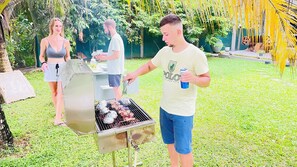 A man grilling food outdoors with a woman and another person in the background. - Villacork (Galle)