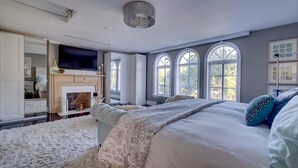 A bedroom with a fireplace, a large bed, a TV, and a view of trees through arched windows. - 4/6bd SPACIOUS, Heart of Miami Beach! Mediterranean Villa w/Jacuzzi, HUGE YARD! (Miami Beach)