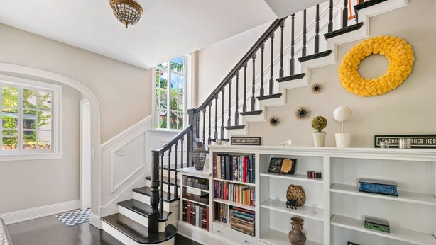 A staircase with a black railing, a bookshelf with books and decorative items, and a yellow wreath on the wall. - 4/6bd SPACIOUS, Heart of Miami Beach! Mediterranean Villa w/Jacuzzi, HUGE YARD! (Miami Beach)