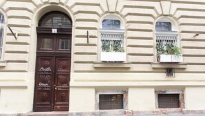 Un edificio con un amplio puerta de arco, dos ventanas con barandillas blancas, y una pequeña ventana con celosía de metal.