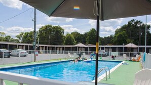 A swimming pool with a green deck and white lounge chairs. There are buildings in the background with a 'No Driving' sign. - Current River Inn (Van Buren)