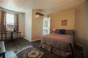Un dormitorio con cama, escritorio y silla. Hay una ventana con cortinas, un radiador y un estante en la pared con una toalla.