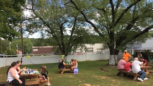 A group of people sitting at picnic tables outdoors, surrounded by trees and a fenced area. - Current River Inn (Van Buren)