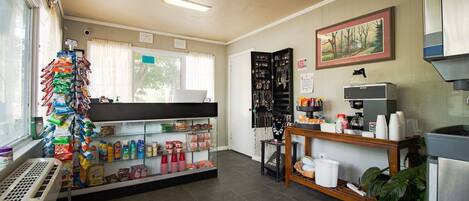 A small, well-lit shop with a variety of snacks and drinks on shelves, a jewelry display, and a coffee machine.