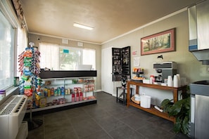 Un petit magasin bien éclairé, avec une variété de collations et de boissons exposées sur des étagères, un présentoir à bijoux et un appareil à café.
