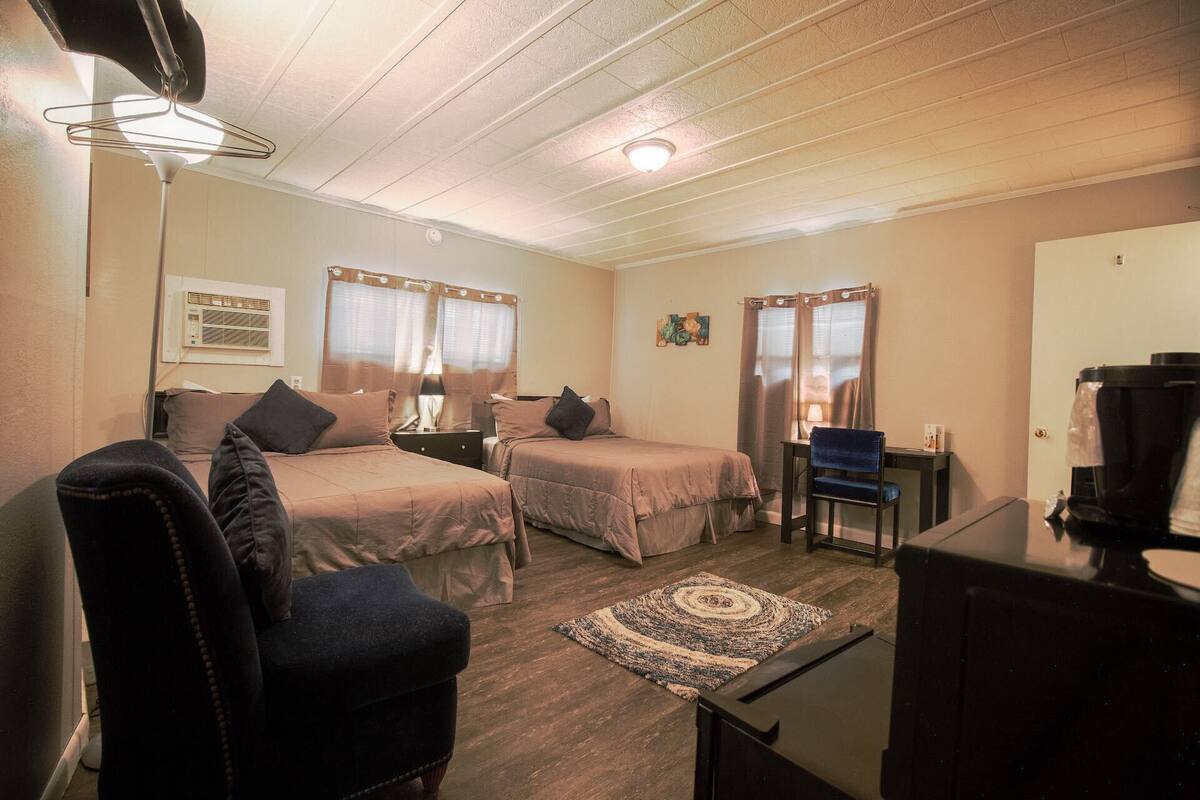 A room with two beds, a desk, a chair, a TV, and a ceiling fan.