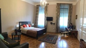 A bedroom with a bed, a desk, a chair, a TV, and a chandelier. - Diamonds Apartments (Budapest)