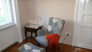 A room with a houndstooth patterned armchair and ottoman, a small table with a lamp, and a radiator. - Diamonds Apartments (Budapest)