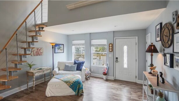 Una habitación amplia con una escalera de madera, una cama con una manta colorida, un sofá blanco y una pequeña mesa con una lámpara.
