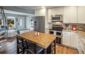 A kitchen with white cabinets, stainless steel appliances, a wooden dining table, and a view of the outside.