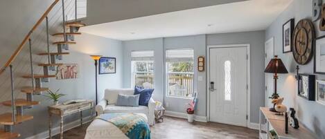 A spacious room with a wooden staircase, a bed with a colorful blanket, a white sofa, and a small table with a lamp.