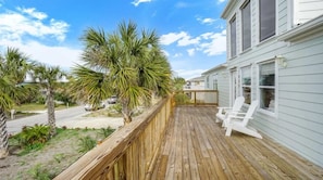 A wooden deck with white chairs, a wooden fence, and palm trees.