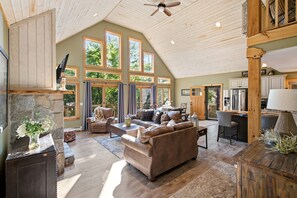 A spacious living room with a high ceiling, large windows, and a cozy seating area.