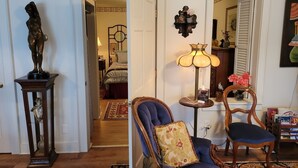 Una sala de estar con una estatua sobre un pedestal, una lámpara, un sillón y una estantería.