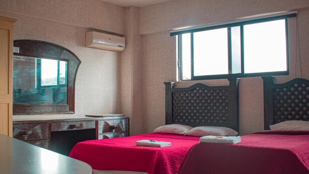 A hotel room with two beds, a desk, a chair, a window, and an air conditioning unit. - Hotel Siesta (Ixtaczoquitlán)