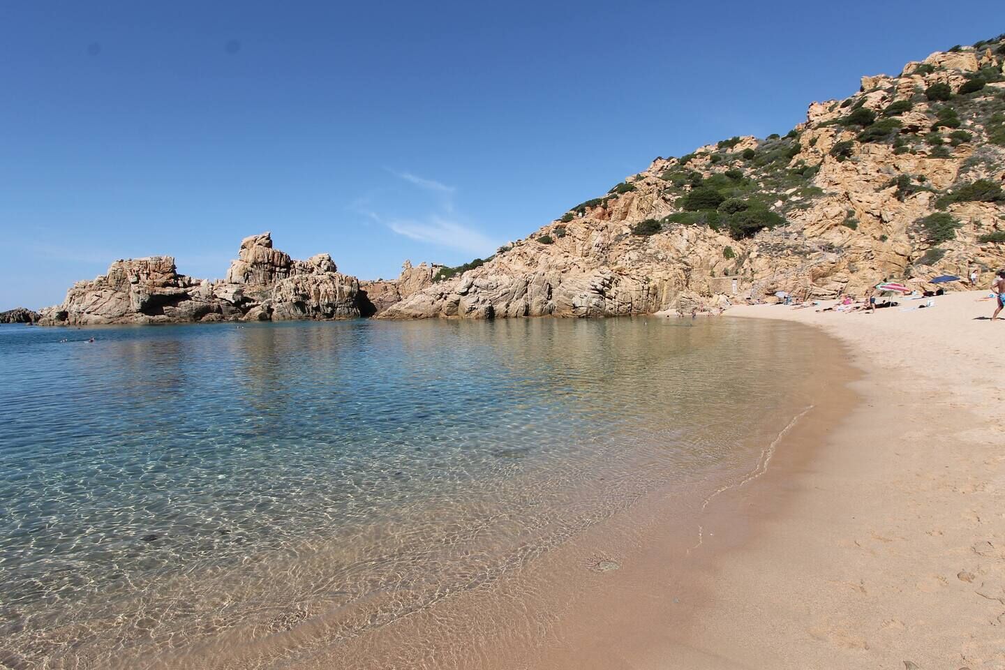 Ein Strand mit klarem Wasser, felsigen Klippen und einem sandigen Ufer.