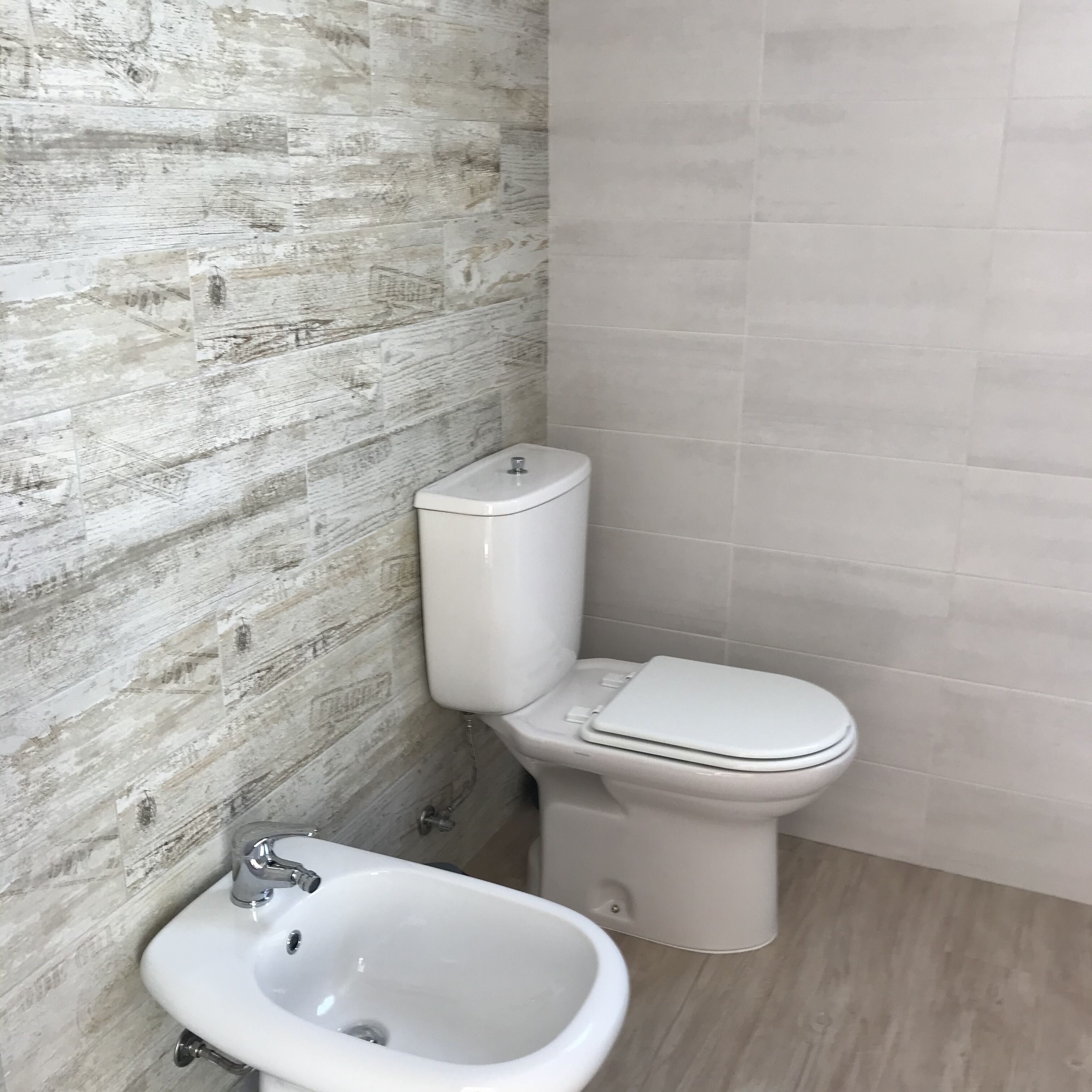 A bathroom with a wooden-textured wall, a white toilet, and a white sink.