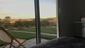 A bedroom with a large window overlooking a grassy area and distant hills. - Monte do Mosteiro CountryHouse (Batalha)
