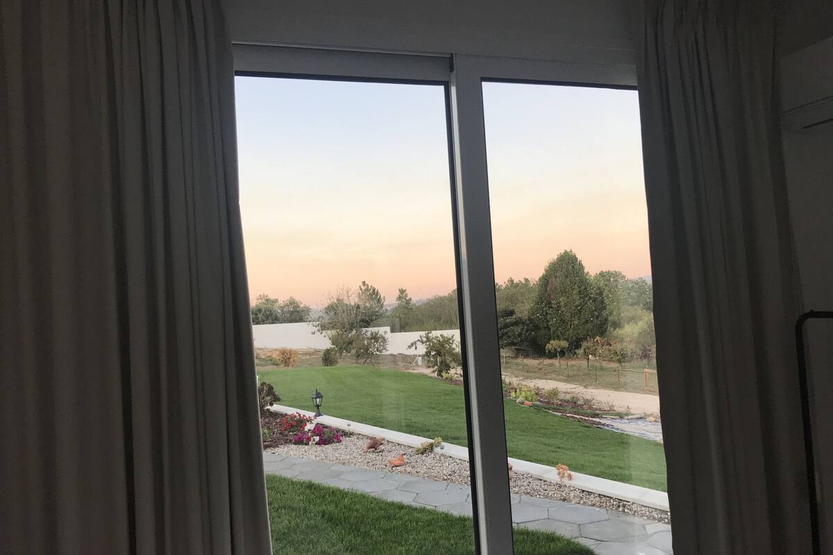 A view through a sliding glass door to a well-maintained outdoor area with a lawn, garden beds, and a paved walkway.