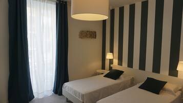 A hotel room with two beds, a large window with curtains, a wall-mounted lamp, and a striped wall design.