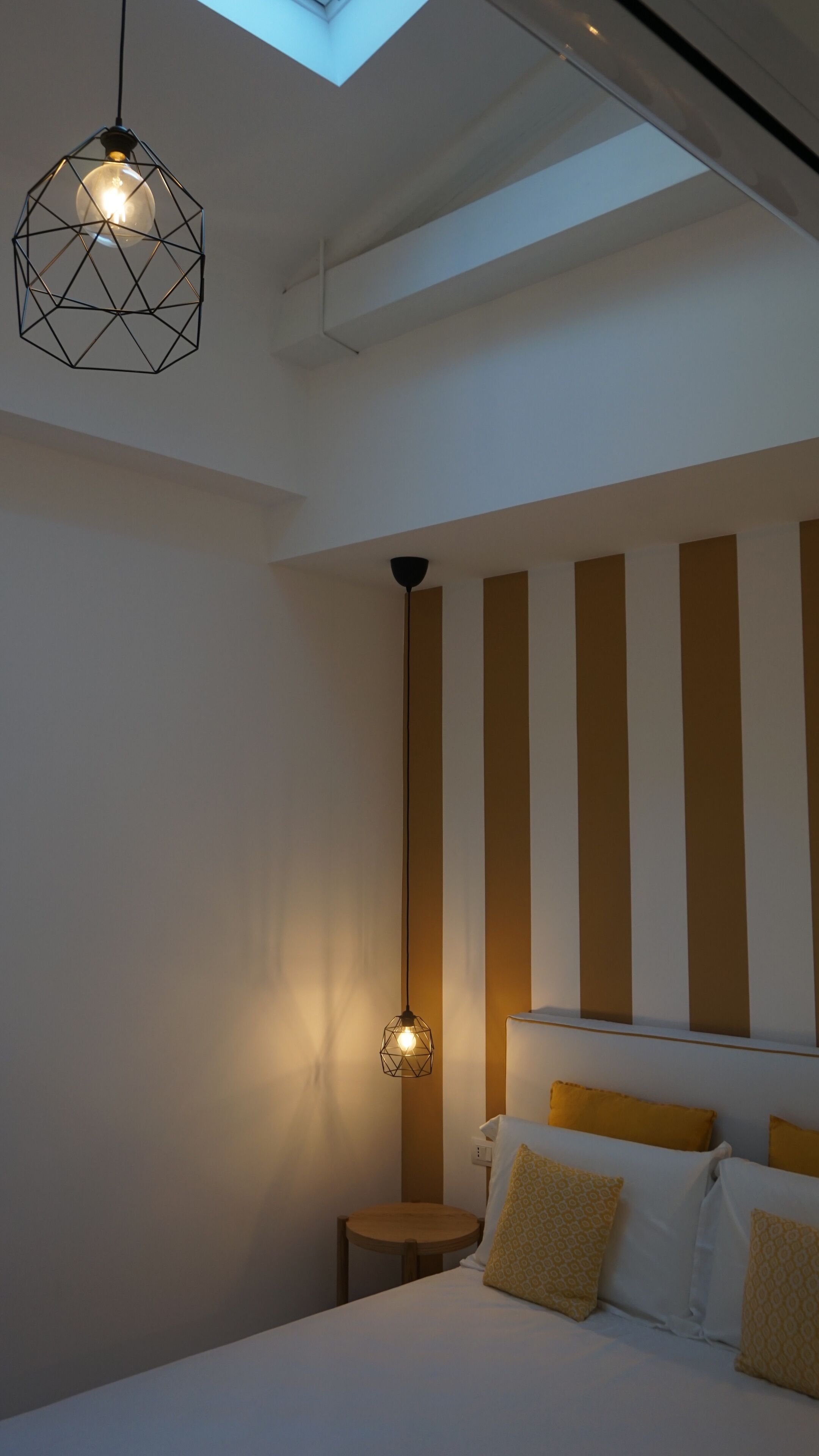 A bedroom with a bed, two bedside tables, and a geometric pendant light.