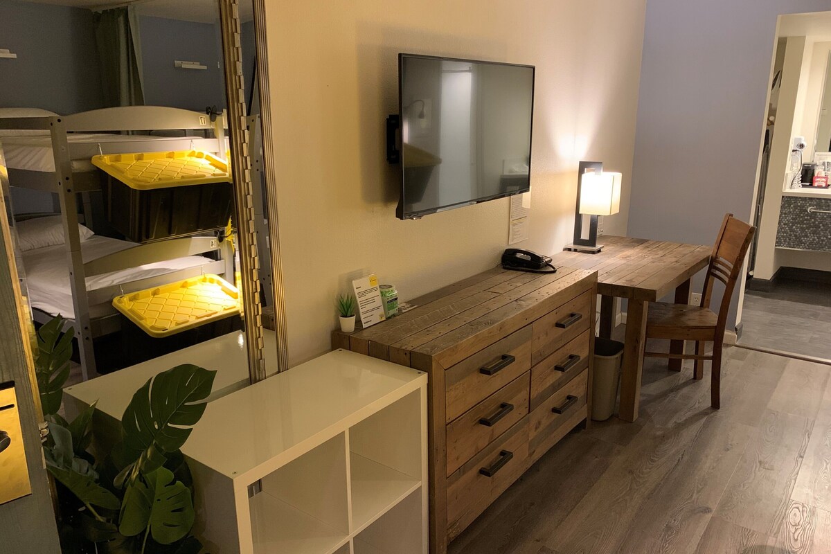 A hotel room with bunk beds, a desk with drawers, a flat-screen TV, a lamp, and a potted plant.