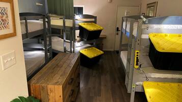 A dormitory room with bunk beds, a wooden bench, and a potted plant.