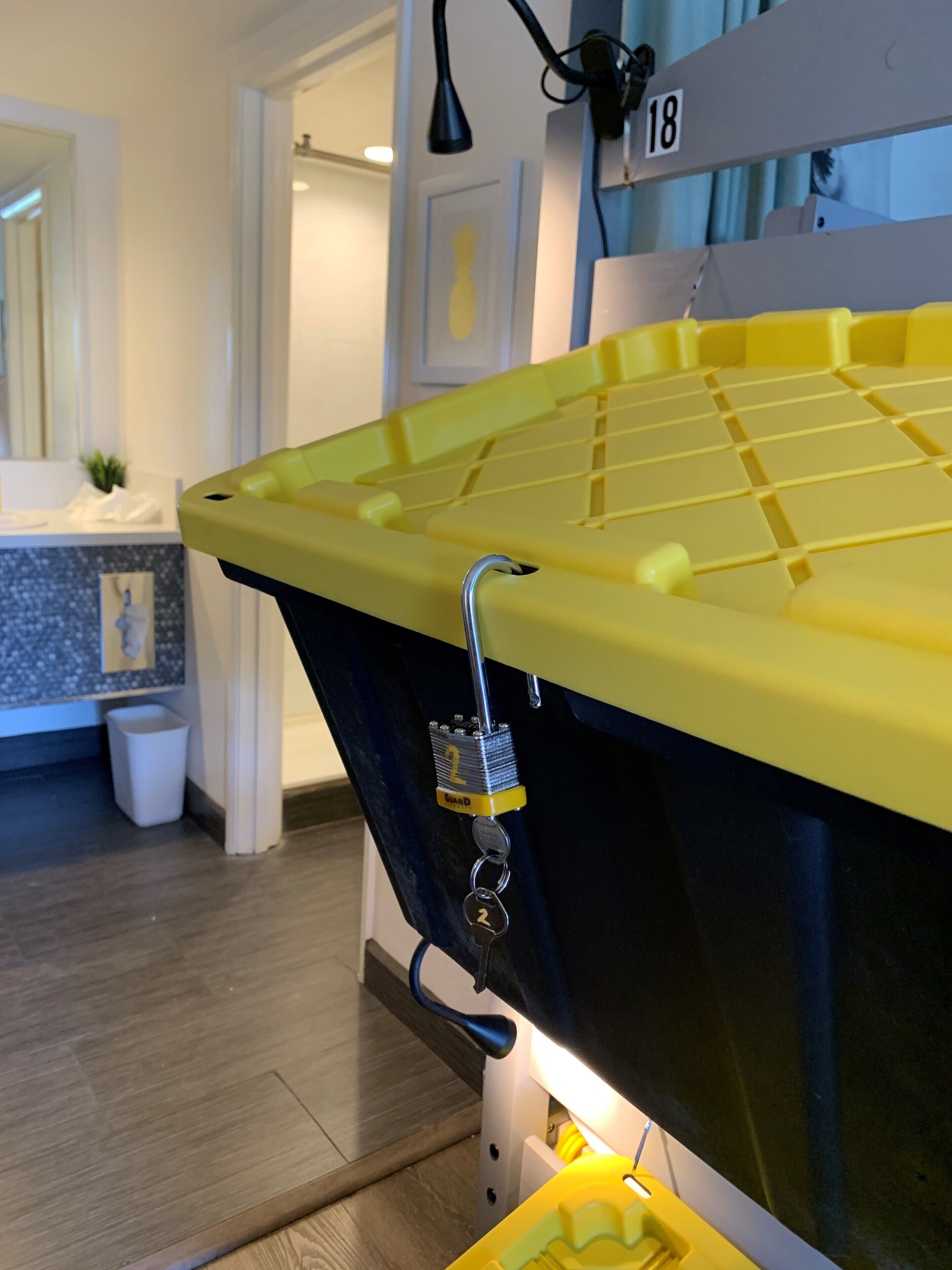 A yellow bathtub with a lock, a white trash bin, and a number 18 sign in a bathroom.