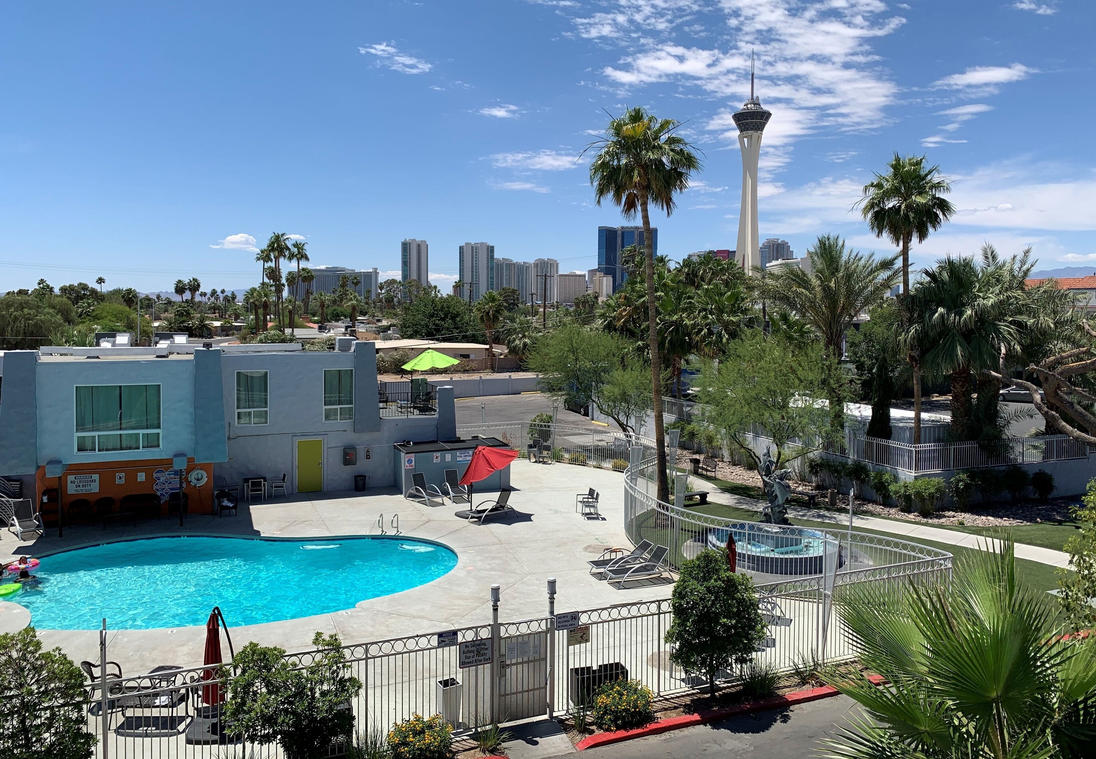 A hotel with a swimming pool, palm trees, and a view of a city skyline including a tall tower.