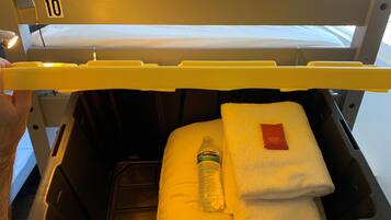 Una cama de hospital con cabecera amarilla, almohada blanca, toalla blanca doblada y una botella de agua Kirkland.