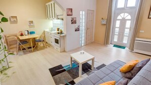 A cozy living room with a sofa, a small table, and a kitchen area with cabinets and a dining table.