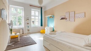 A bedroom with a bed, a bedside table, a radiator, a window with curtains, and wall art.