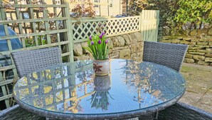 A round glass table with wicker chairs, a potted plant with purple flowers, and a stone wall in the background. - 2 bedroom accommodation in Redmire, near Leyburn (Redmire, near Leyburn)