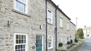 A stone building with multiple windows and doors, a sign indicating 'Sweet Inn Cottages,' and a narrow street. - 2 bedroom accommodation in Redmire, near Leyburn (Redmire, near Leyburn)