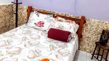 Uma cama com colcha estampada em flor, um travesseiro vermelho e duas toalhas enroladas.