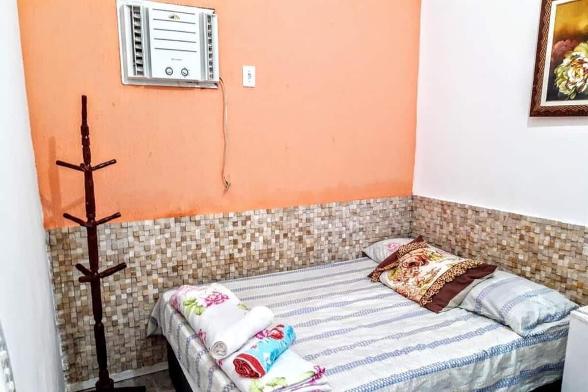 A bedroom with a bed, a wall-mounted air conditioning unit, a tiled lower wall, and a framed picture on the wall.