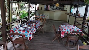 An outdoor dining area with tables and chairs, covered by a wooden structure with a view of the garden. - Pousada L'Auberge (Angra dos Reis)