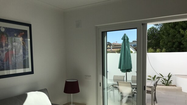 A modern living room with a sofa, a lamp, and a sliding glass door leading to an outdoor patio with chairs and an umbrella. - New and complete house, 300 mtrs from Manta Rota beach (Vila Nova de Cacela)