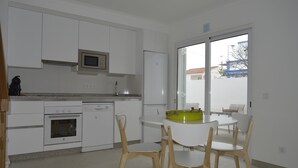 A modern kitchen with white cabinets, a microwave, a refrigerator, an oven, and a dishwasher. There is a round table with chairs in front of a large window. - New and complete house, 300 mtrs from Manta Rota beach (Vila Nova de Cacela)